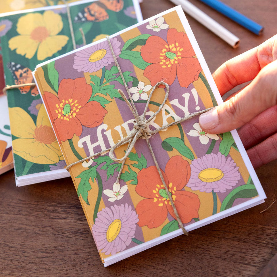 Fun floral and striped greeting card with 'Hurray' text, tied with string, on a wooden surface.