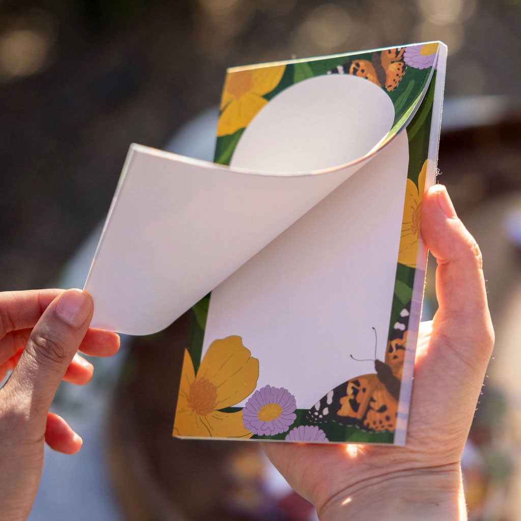 Floral notepad held by hands with a soft nature outdoor background