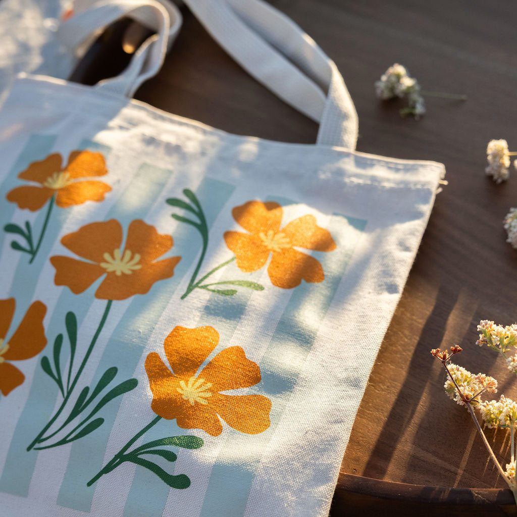 Tote bag with orange poppy design and sage stripes on a wooden surface