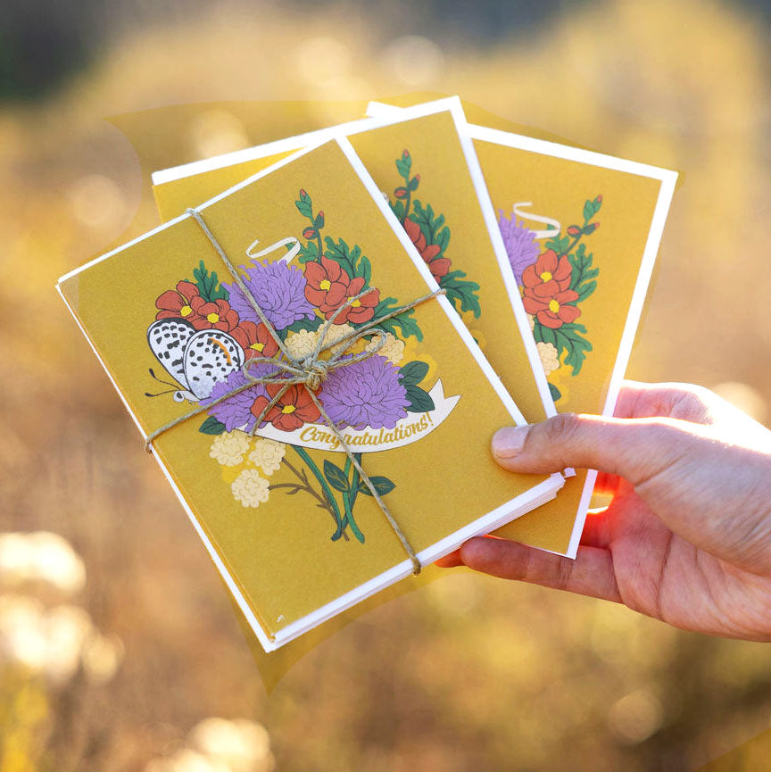 Hand holding three floral greeting cards with a blurred natural california background