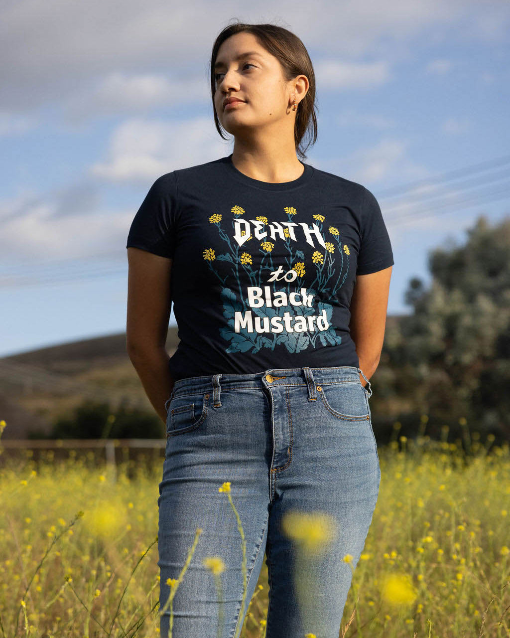 Person wearing the Death to Black Mustard T-shirt, standing in a field of mustard plants, raising awareness about invasive species.