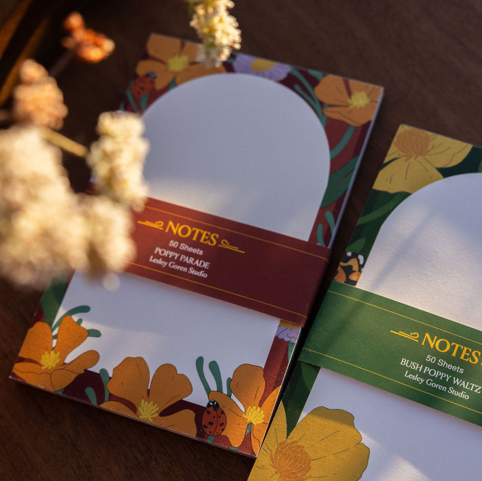 Burgundy notepad with floral designs and 'NOTES' text on a wooden surface