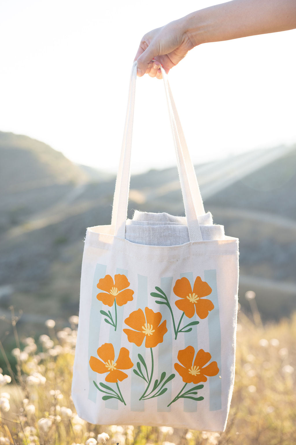 Tote bag with orange floral design held by a hand against a natural background