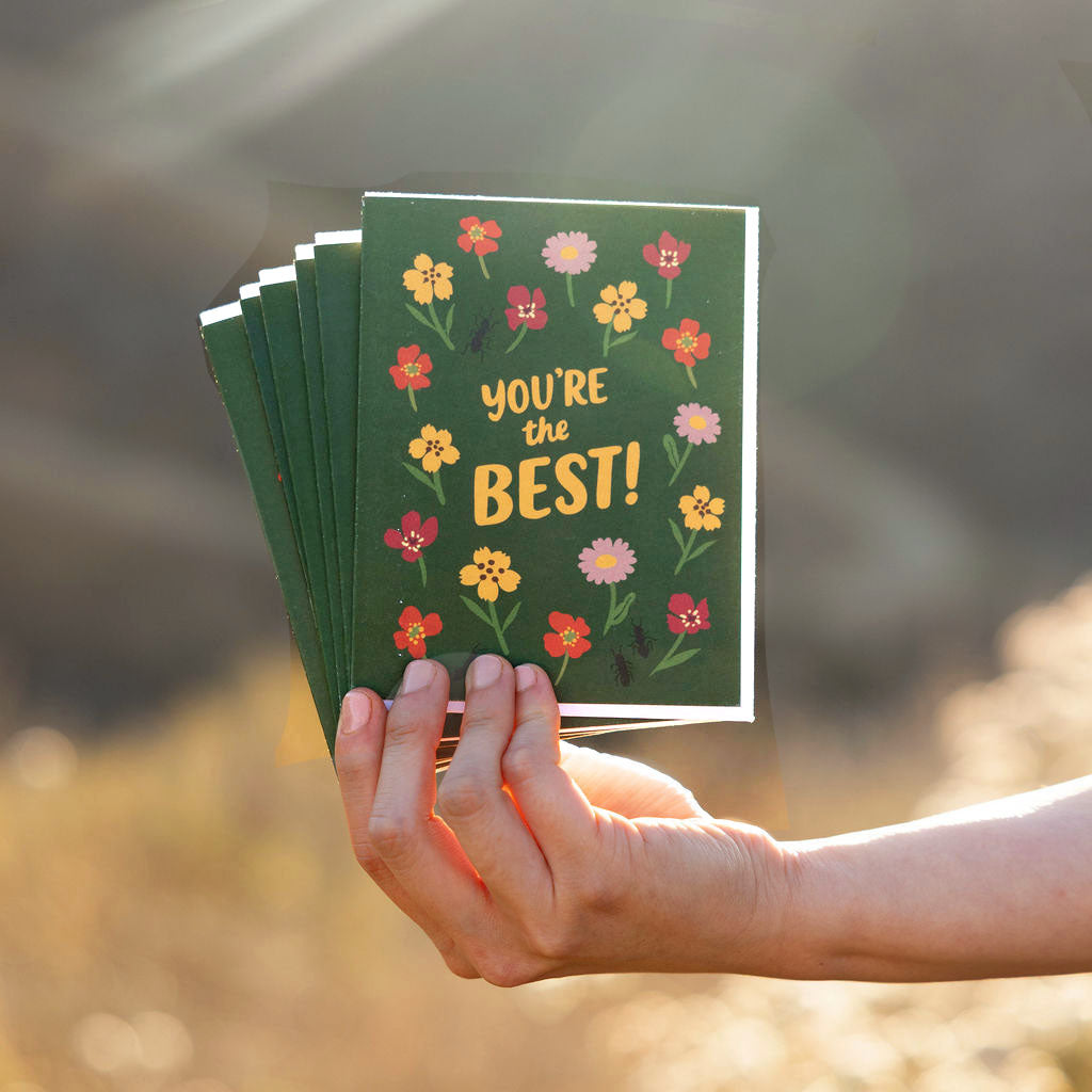 Hand holding a stack of eco-friendly green cards with cute fun floral designs and 'You're the Best!' text.