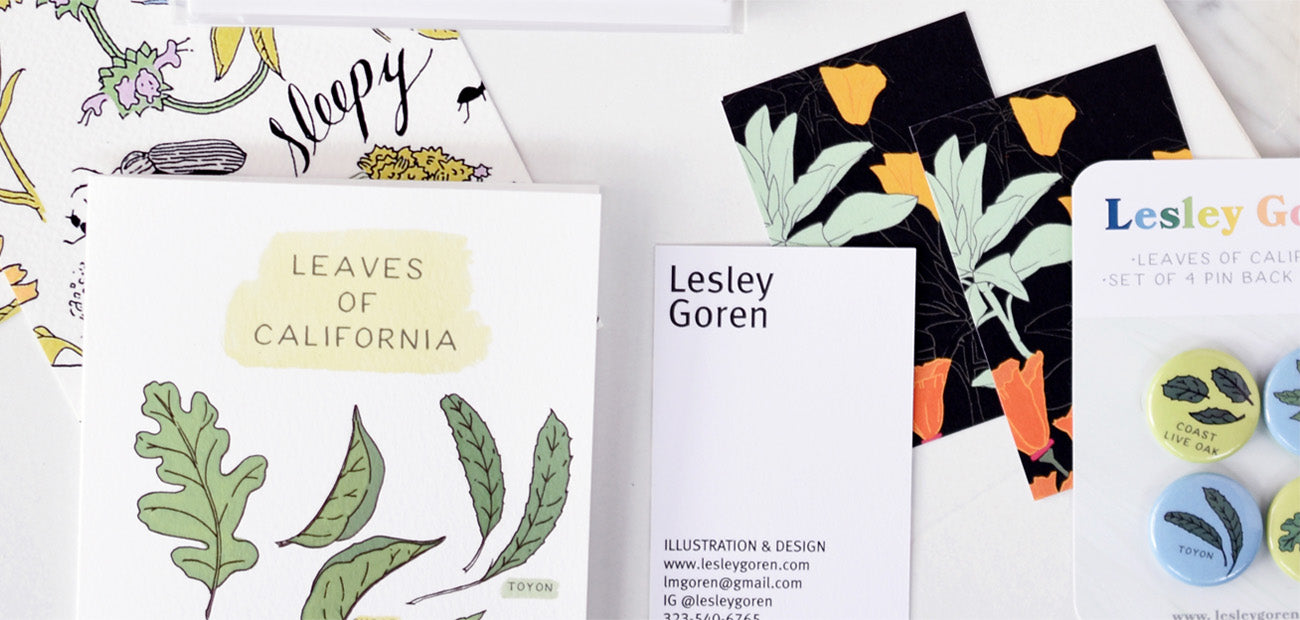 flat lay of cards, business cards, and pins with illustrated designs